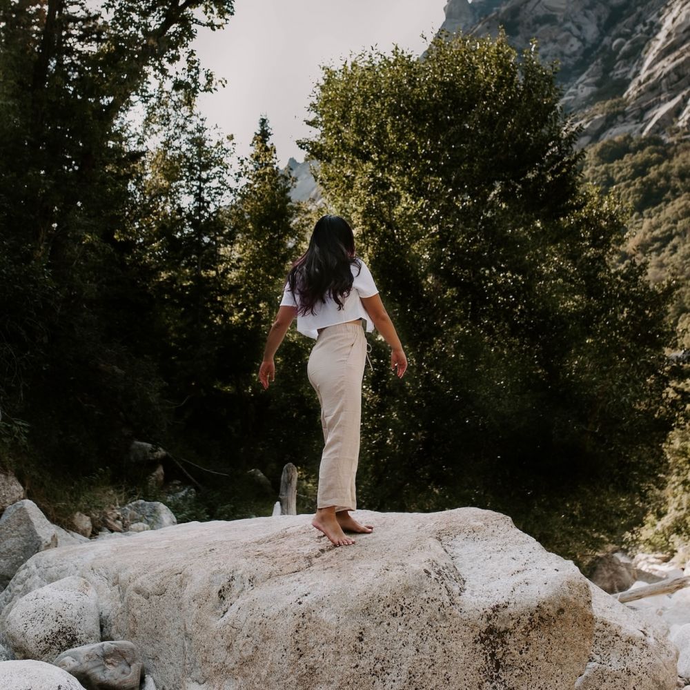 Woman standing on a rock turned towards a beautiful pine tree forest