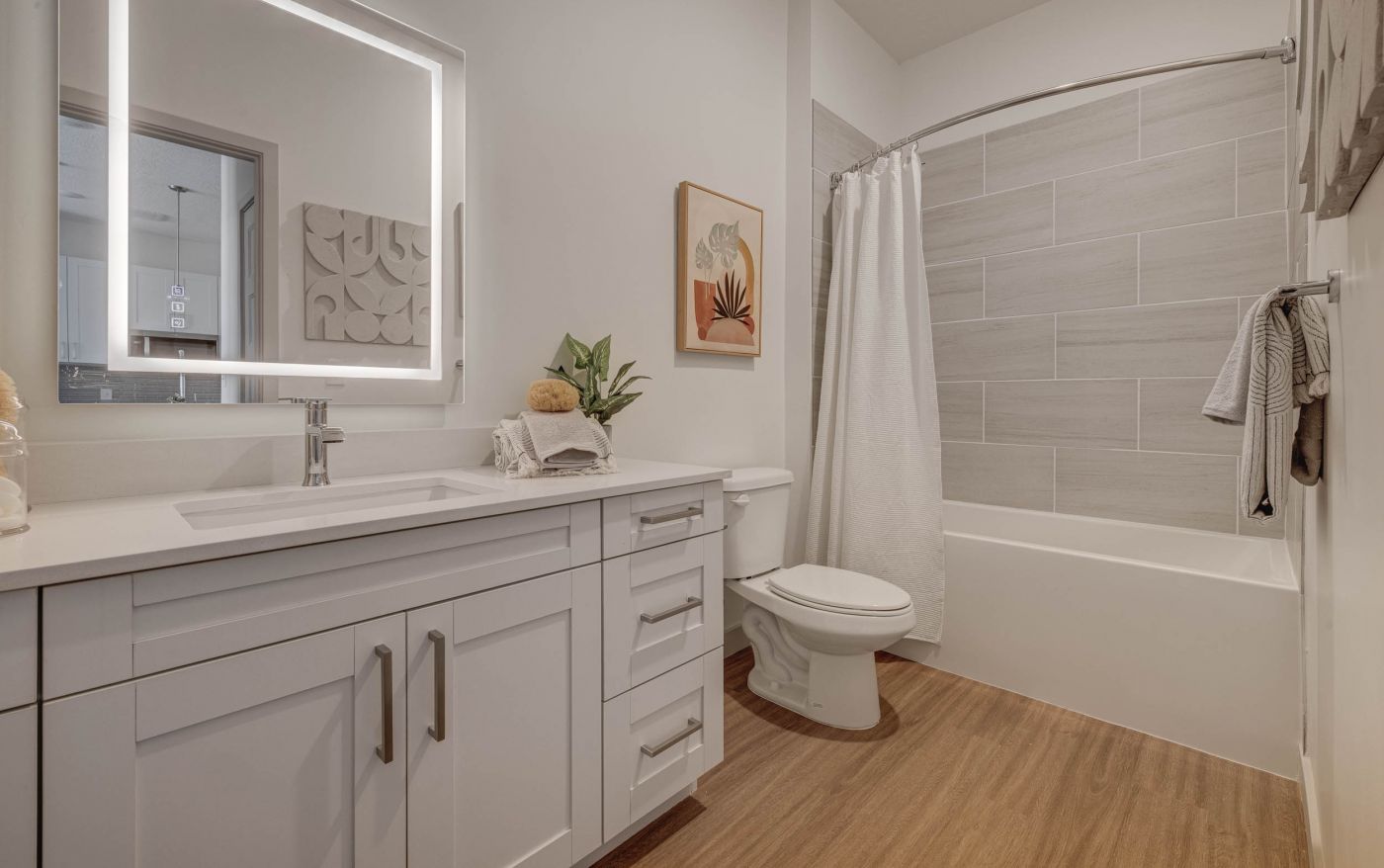 Modern bathroom with white vanity, lighted mirror, and tub with tile surround at Alta Stone at The Gateway apartment.
