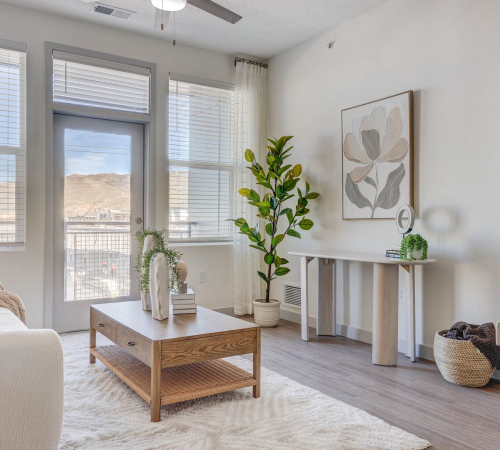 Bright, modern living area with large windows, wooden coffee table, and greenery at Alta Stone at The Gateway apartment.